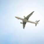 A white commercial airplane flying high against a clear blue sky, showcasing aviation dynamics.