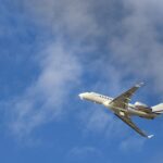 Commercial jet airplane flying high with a clear blue sky and clouds in the backdrop.